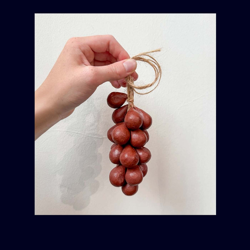 Hand holding a small soap shaped as a grapes on a white background