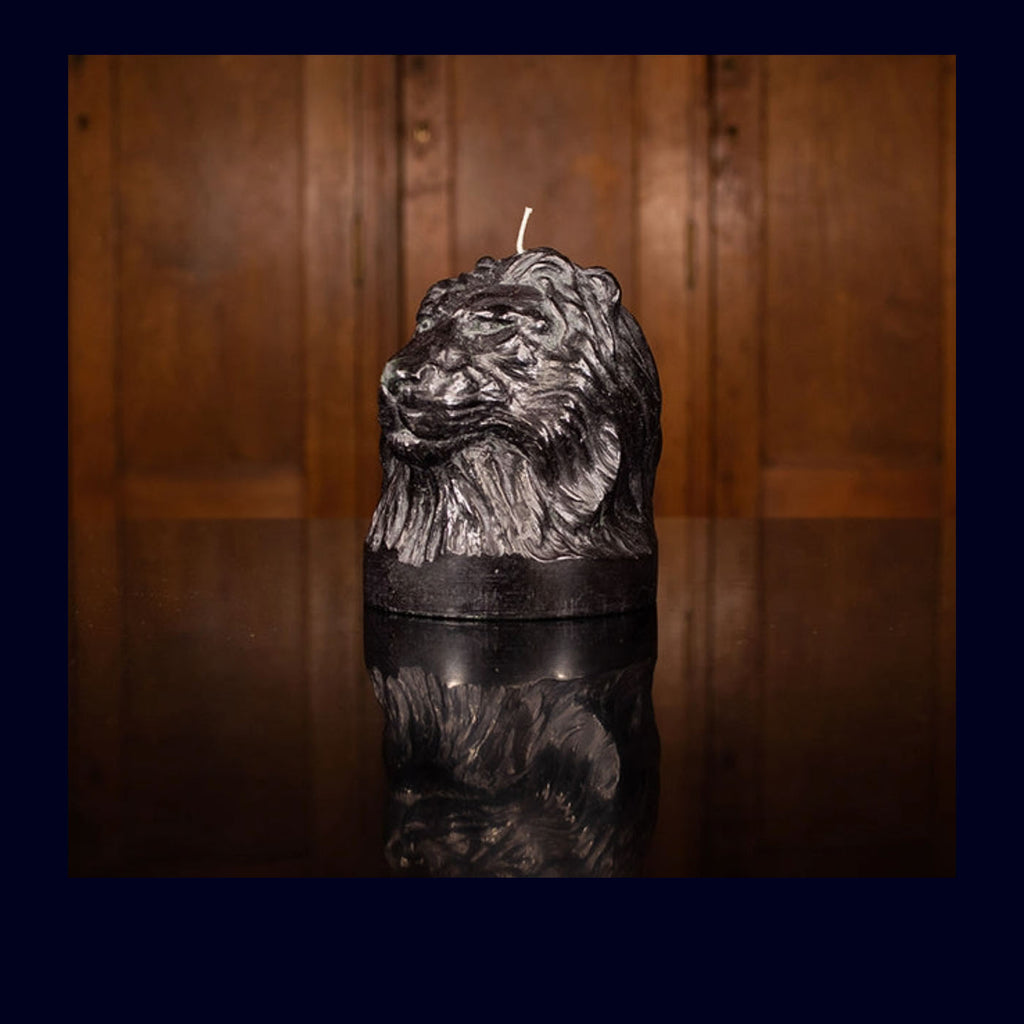 Black candle with a lion head design on a reflective surface with a wooden background