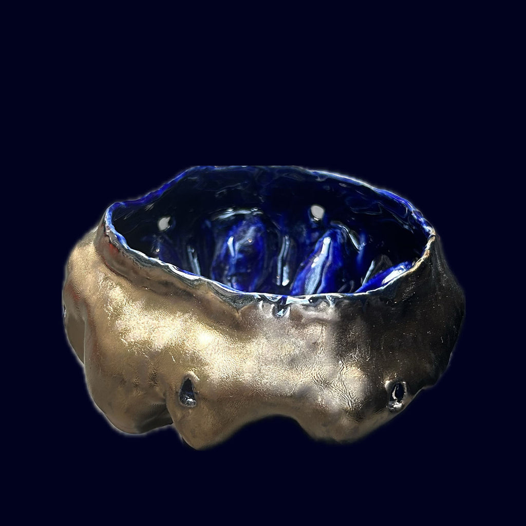 Ceramic bowl with blue interior and textured gold exterior on a black background