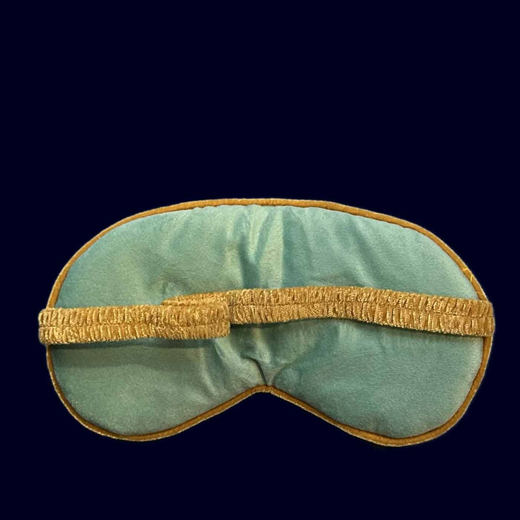 Teal eye mask with gold trim on a dark blue background