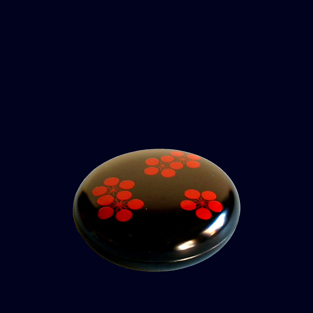 Round black lacquer box with red floral patterns on a dark background