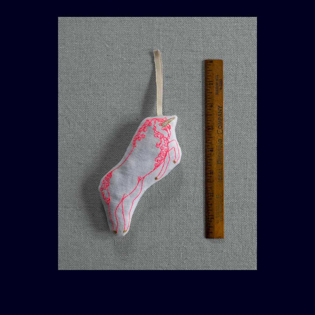 Decorative sachet with pink and white design on a gray background with a ruler for scale.