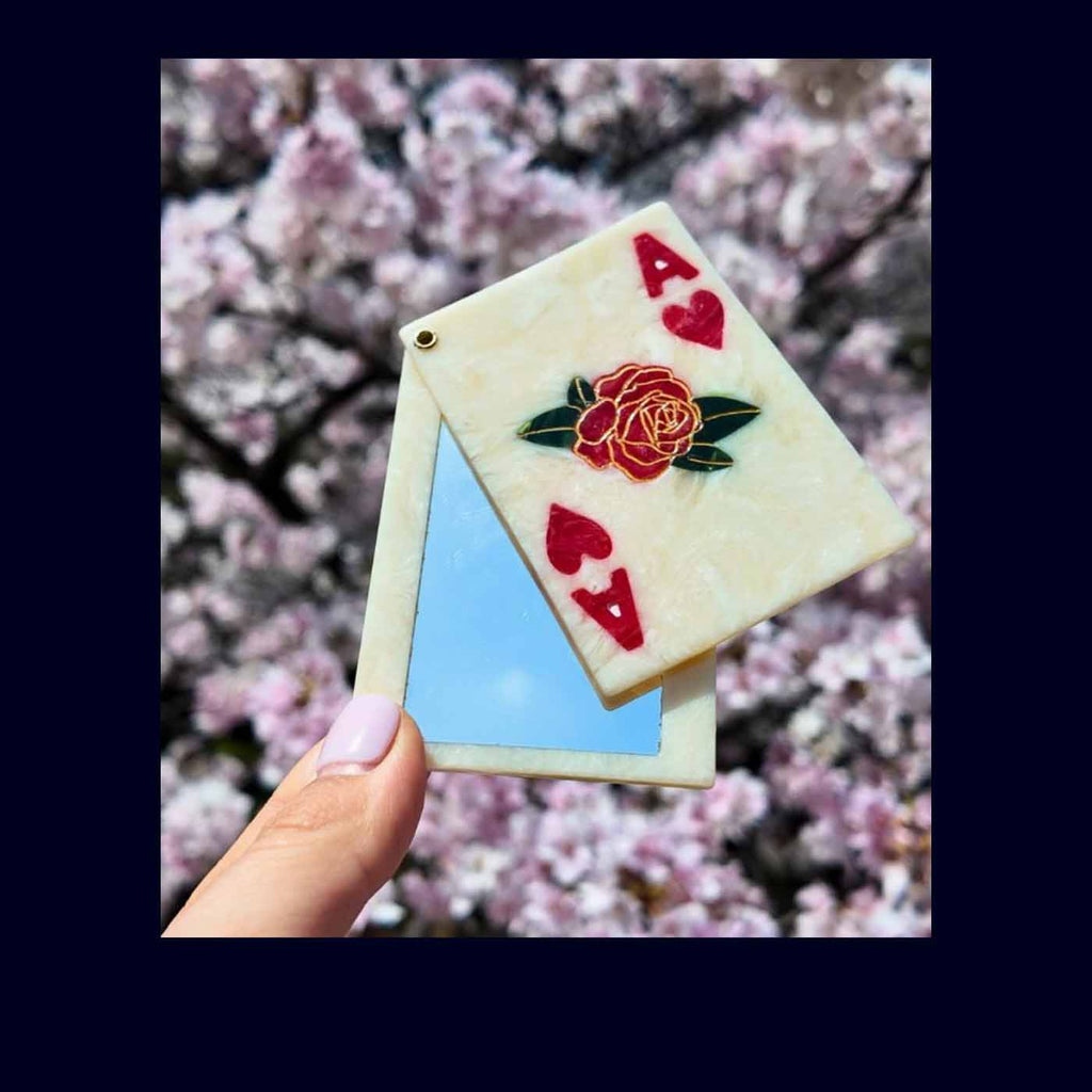 compact mirror with roses and hearts held against a cherry blossom background