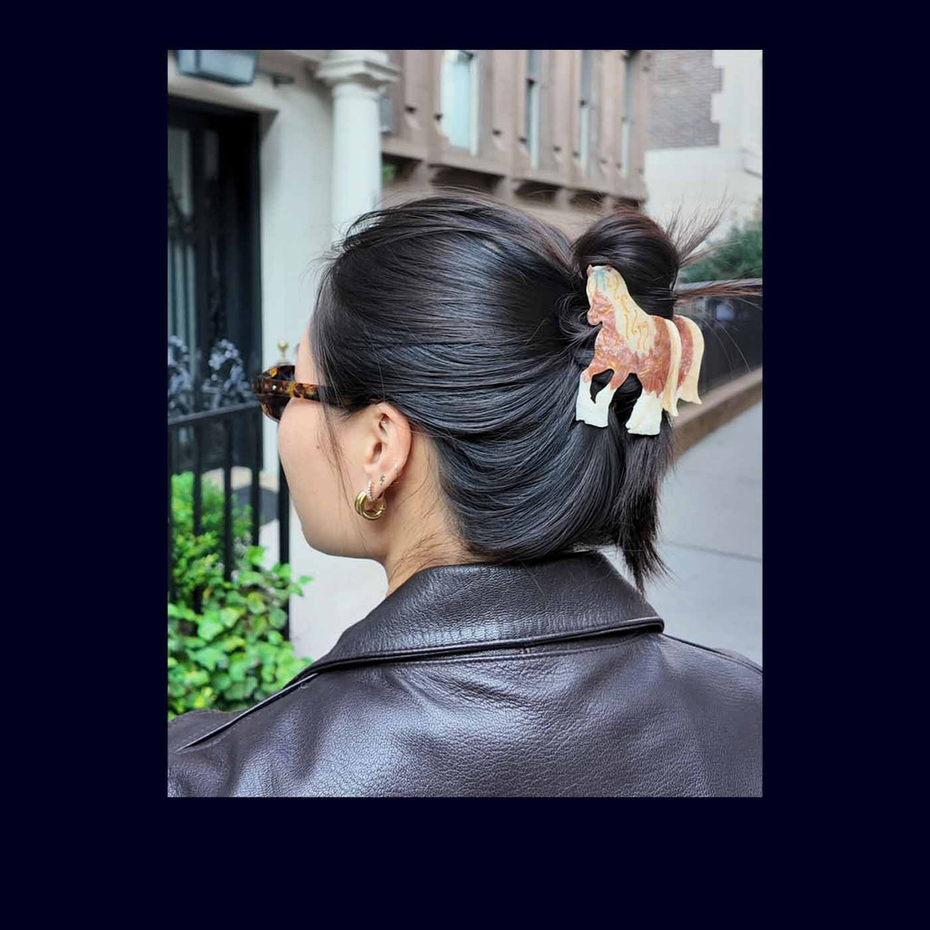 Person with stylish hair and accessories, wearing a black leather jacket, in an urban setting.